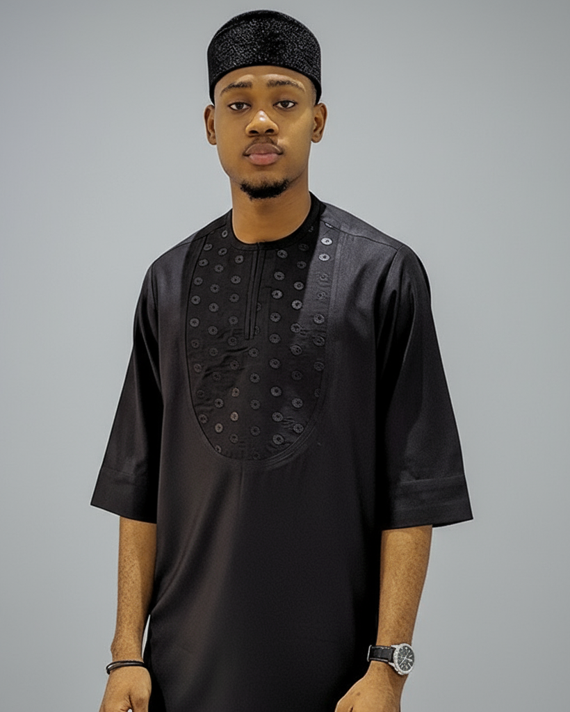 Man wearing a black traditional outfit with intricate designs on a gray background