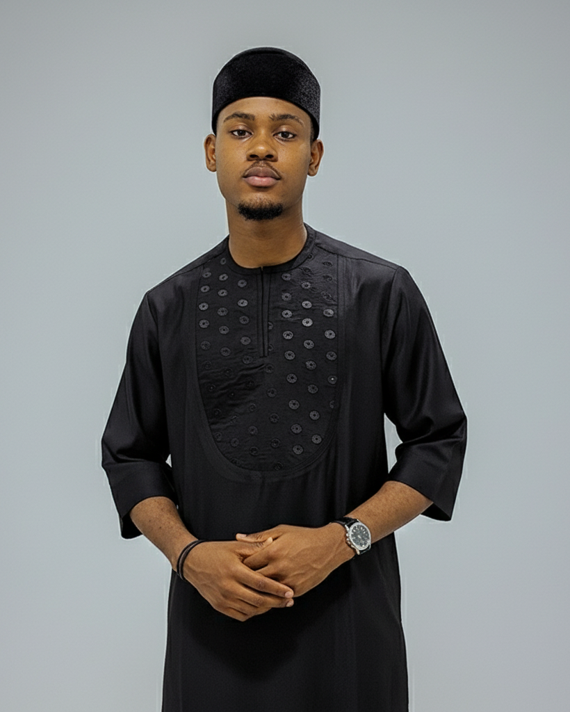 Man wearing a black traditional outfit with a cap on a gray background