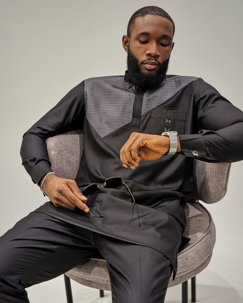 Man in a black outfit sitting on a chair, looking at his watch.