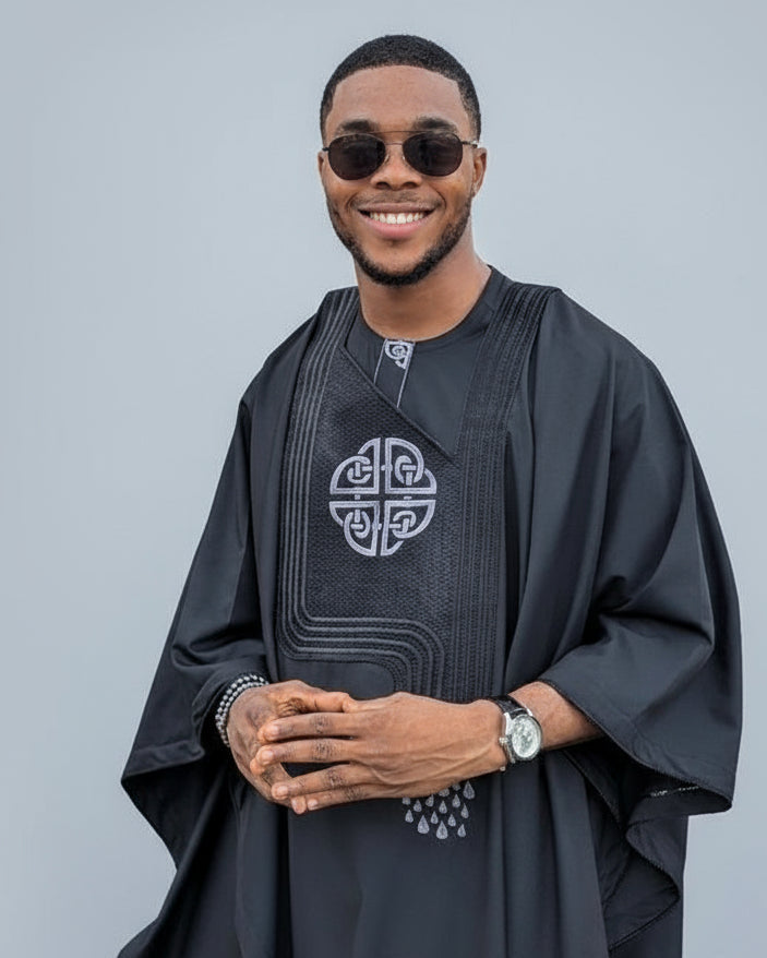 Man wearing a black traditional outfit with intricate designs on a gray background