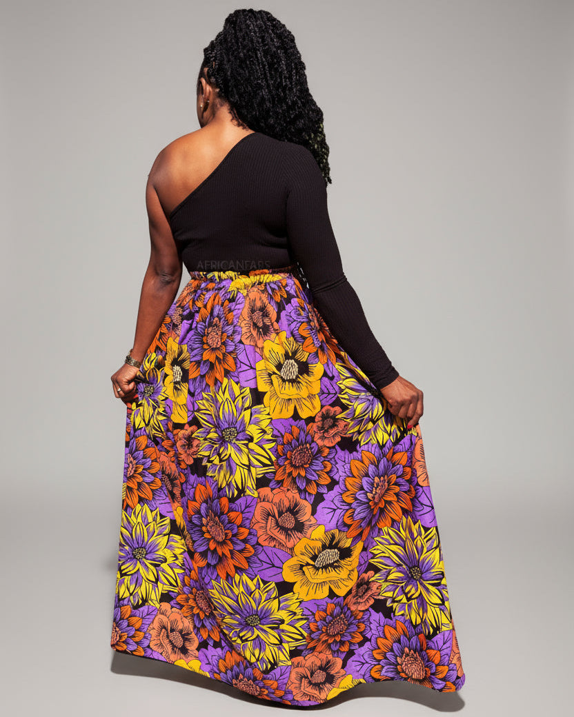 Person wearing a colorful floral skirt and black top in an outdoor setting with greenery.