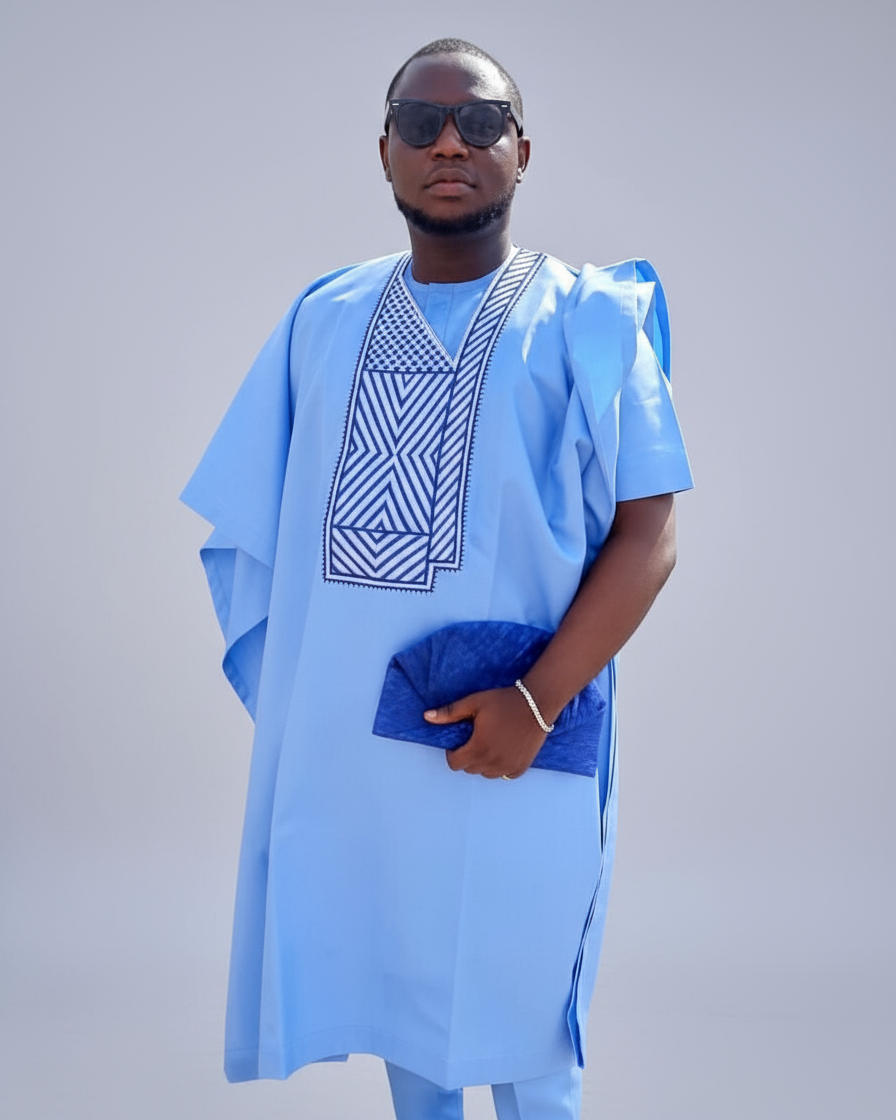 Man wearing a light blue traditional outfit with geometric patterns on a plain background